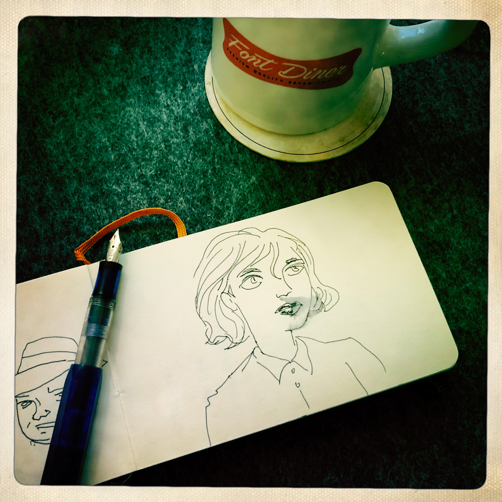 Photo of a coffee cup and a sketchbook. The drawing is of a woman.